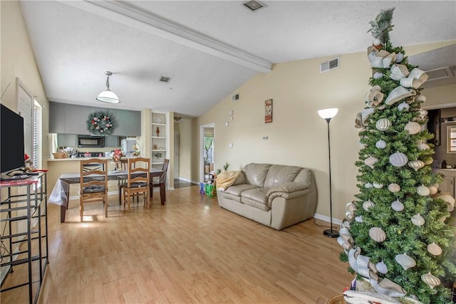 living room with a textured ceiling, lofted ceiling with beams, and light hardwood / wood-style flooring