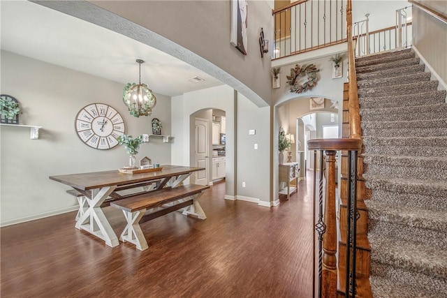 dining space with dark hardwood / wood-style flooring, a towering ceiling, and a chandelier