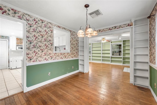 unfurnished dining area featuring built in shelves, crown molding, light hardwood / wood-style flooring, and ceiling fan with notable chandelier