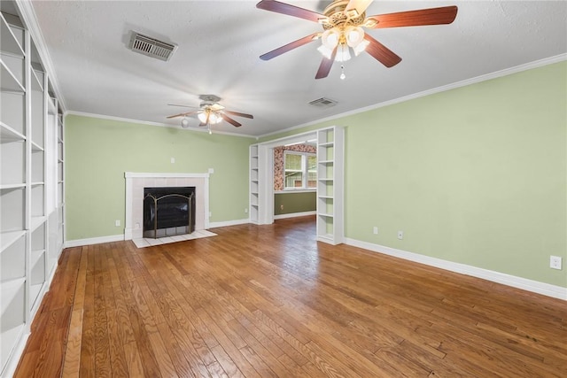 unfurnished living room featuring a tiled fireplace, crown molding, hardwood / wood-style floors, and built in shelves