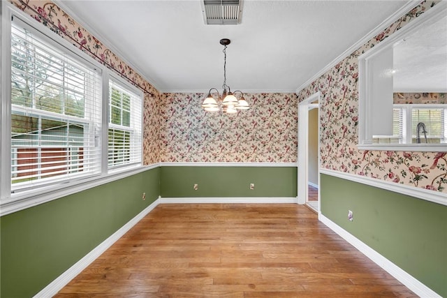 unfurnished dining area featuring hardwood / wood-style floors, crown molding, and a notable chandelier