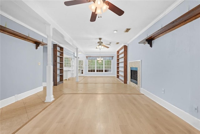 unfurnished living room featuring ceiling fan, crown molding, a tile fireplace, light hardwood / wood-style flooring, and built in features