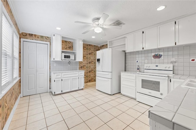 kitchen with white appliances, ceiling fan, light tile patterned floors, tile counters, and white cabinetry