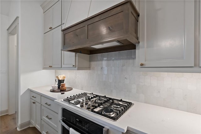 kitchen with oven, light countertops, decorative backsplash, custom exhaust hood, and stainless steel gas cooktop