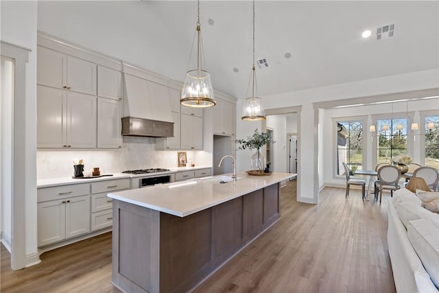 kitchen with premium range hood, tasteful backsplash, visible vents, light wood-style flooring, and light countertops