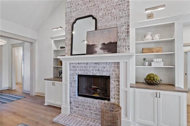 living area with a tile fireplace, wood finished floors, built in features, baseboards, and lofted ceiling