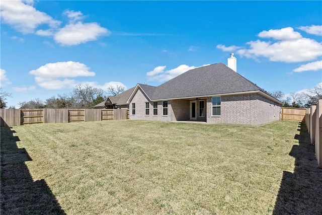 back of house with a chimney, a yard, brick siding, and a fenced backyard