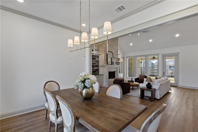 dining area with ceiling fan, visible vents, a brick fireplace, wood finished floors, and vaulted ceiling with beams