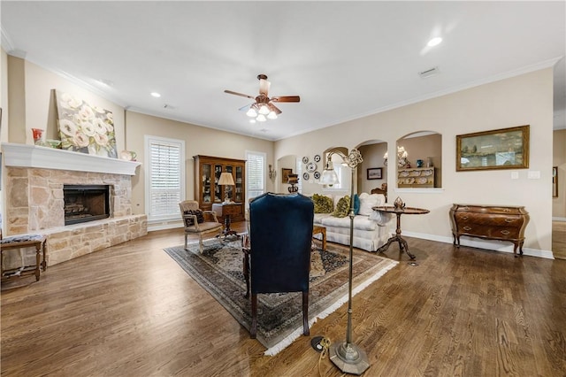 living room featuring hardwood / wood-style floors, a stone fireplace, ceiling fan, and crown molding