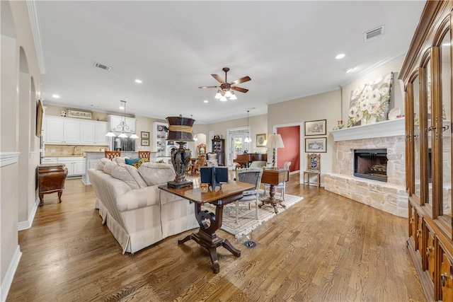 living room featuring ceiling fan, a fireplace, ornamental molding, and light wood-type flooring