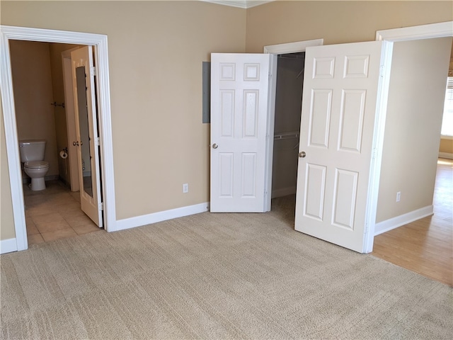 unfurnished bedroom with ensuite bathroom, a closet, a spacious closet, and light carpet