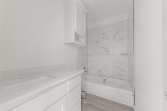 bathroom with wood-type flooring, vanity, and tiled shower / bath