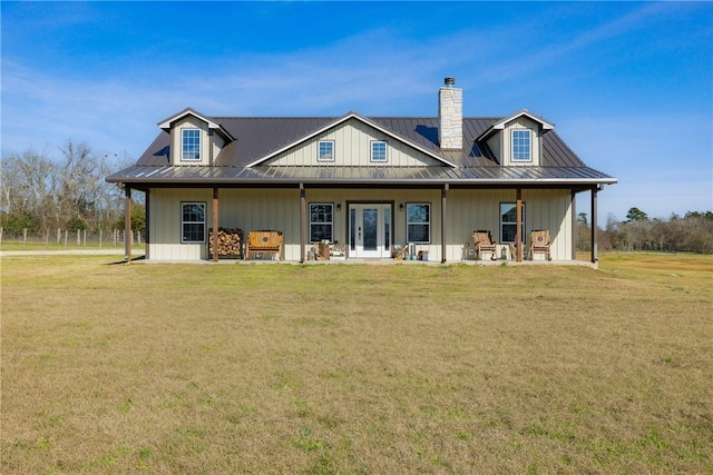 back of property with metal roof, a standing seam roof, a chimney, and a lawn