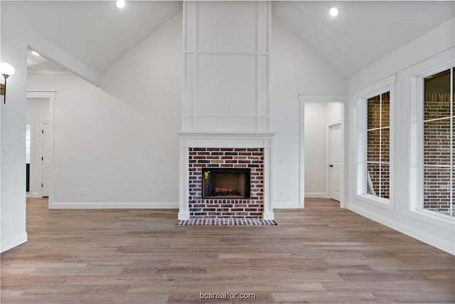 unfurnished living room with light hardwood / wood-style flooring, high vaulted ceiling, and a brick fireplace