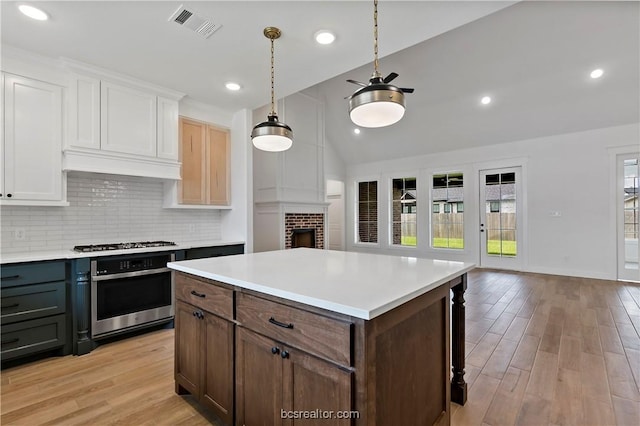 kitchen with white cabinetry, stainless steel appliances, light hardwood / wood-style floors, vaulted ceiling, and a fireplace