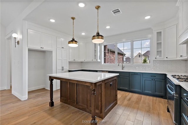 kitchen with light wood-type flooring, backsplash, decorative light fixtures, a center island, and white cabinetry