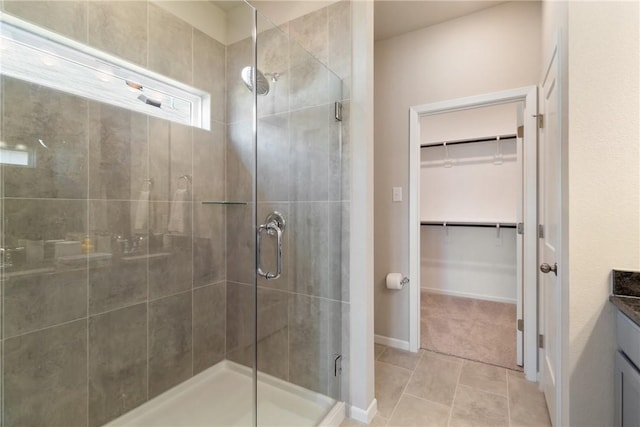 bathroom with a walk in closet, a shower stall, vanity, tile patterned flooring, and baseboards