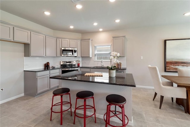 kitchen with a breakfast bar, a center island, stainless steel appliances, tasteful backsplash, and dark stone countertops