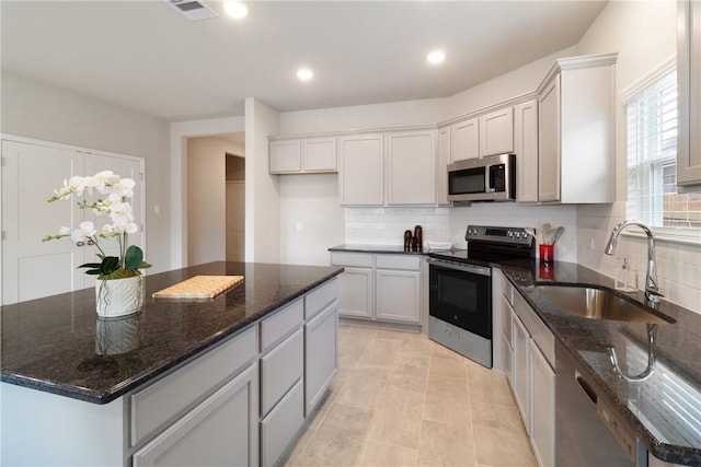 kitchen with visible vents, dark stone countertops, a sink, stainless steel appliances, and backsplash