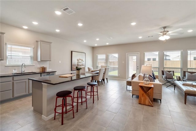 kitchen featuring dark countertops, gray cabinets, visible vents, a kitchen island, and a sink