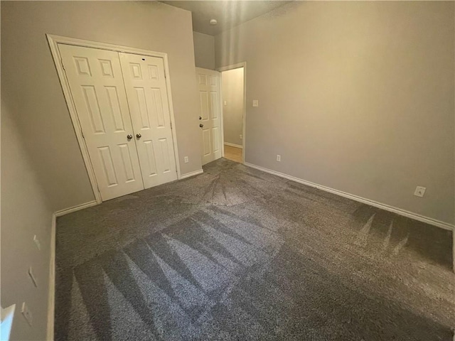 unfurnished bedroom featuring baseboards, dark colored carpet, and a closet