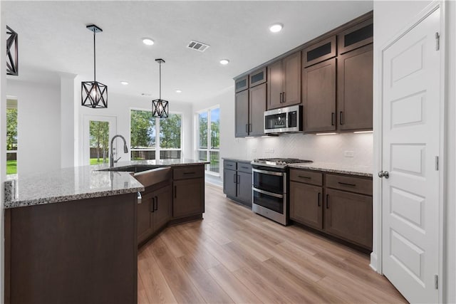 kitchen with pendant lighting, light stone countertops, light wood-type flooring, appliances with stainless steel finishes, and dark brown cabinetry