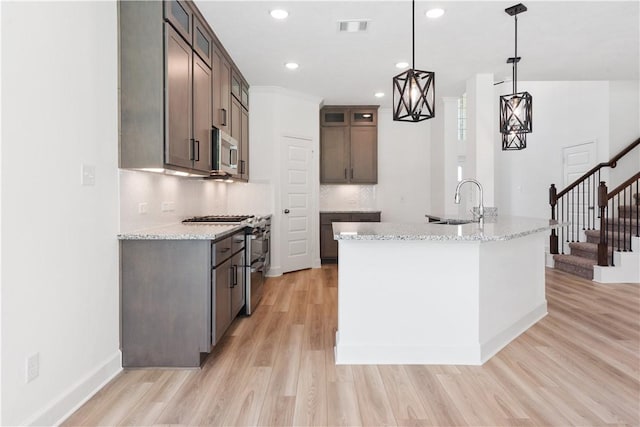 kitchen with light stone countertops, decorative backsplash, light wood-type flooring, stainless steel appliances, and decorative light fixtures