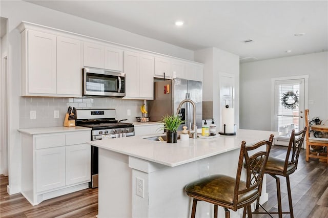 kitchen with appliances with stainless steel finishes, backsplash, white cabinetry, and a kitchen island with sink