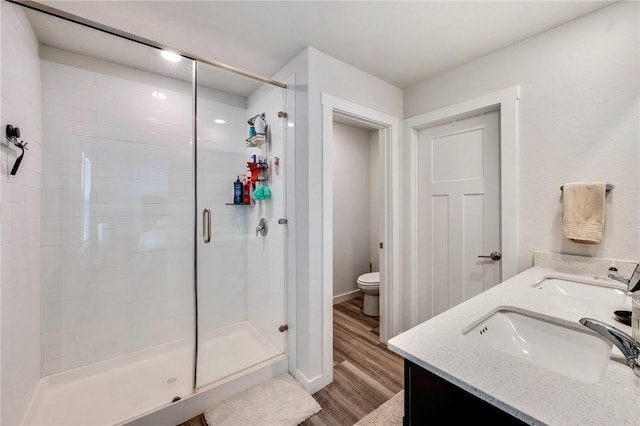 bathroom with hardwood / wood-style floors, toilet, a shower with door, and vanity