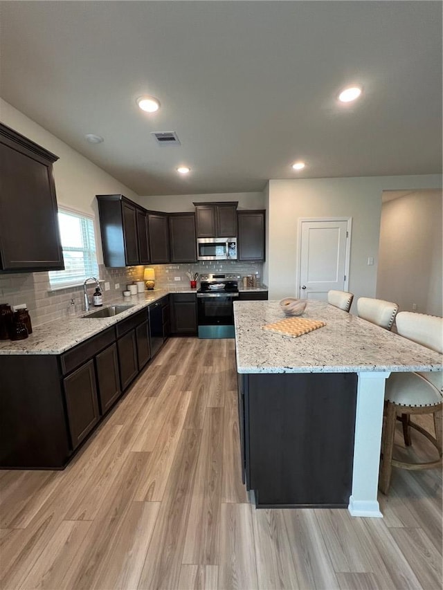 kitchen featuring sink, appliances with stainless steel finishes, a center island, a kitchen bar, and light wood-type flooring