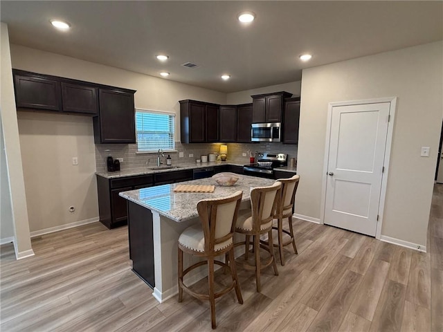 kitchen featuring sink, stainless steel appliances, a center island, light hardwood / wood-style floors, and light stone countertops