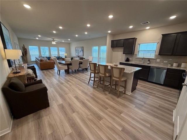 kitchen featuring a breakfast bar, light stone counters, tasteful backsplash, a center island, and stainless steel dishwasher