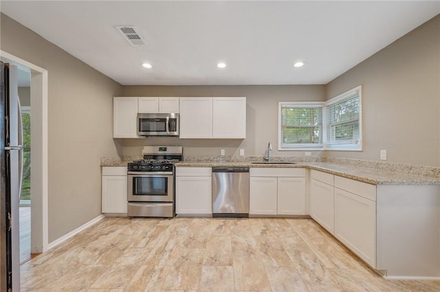 kitchen featuring sink, light stone counters, light hardwood / wood-style floors, white cabinets, and appliances with stainless steel finishes