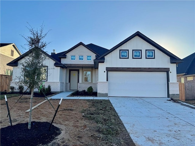 view of front of house with board and batten siding, brick siding, driveway, and fence