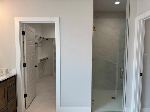 bathroom featuring a walk in closet, vanity, marble finish floor, and a marble finish shower