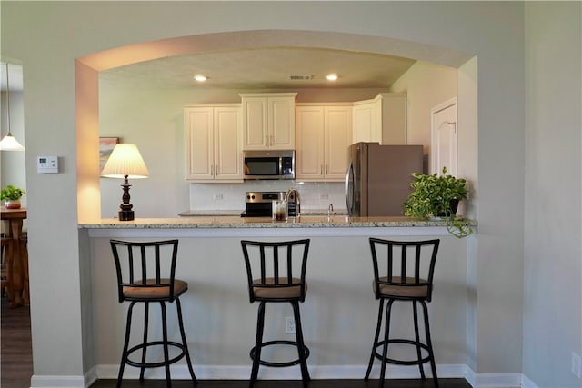 2011 Stubbs Dr, Bryan, TX 77807 - kitchen with freestanding refrigerator, stainless steel microwave, tasteful backsplash, light stone countertops, and arched walkways