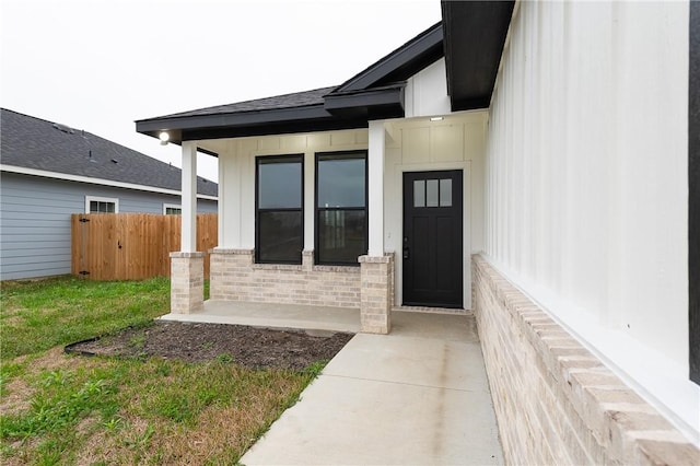 doorway to property featuring fence, a yard, board and batten siding, a shingled roof, and brick siding