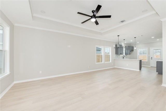 unfurnished living room featuring a tray ceiling, ornamental molding, and light wood finished floors