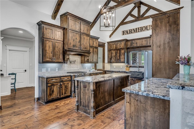 kitchen with light stone countertops, beam ceiling, a center island, and dark brown cabinets