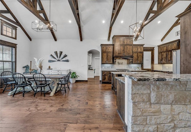 kitchen with backsplash, dark wood-type flooring, decorative light fixtures, light stone counters, and stainless steel refrigerator