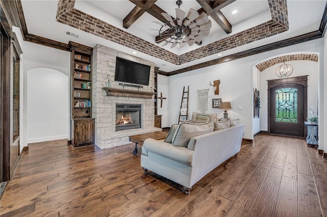 living room featuring dark hardwood / wood-style flooring, coffered ceiling, ceiling fan with notable chandelier, beamed ceiling, and a stone fireplace