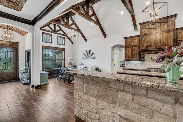 kitchen featuring light stone countertops, beamed ceiling, high vaulted ceiling, decorative light fixtures, and decorative backsplash