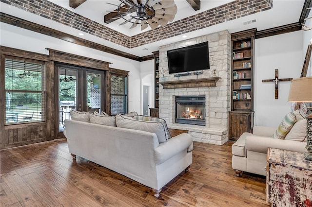 living room with a stone fireplace, ceiling fan, wood-type flooring, and ornamental molding