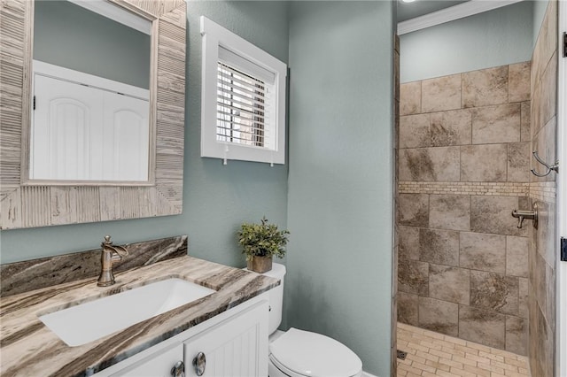 bathroom with a tile shower, vanity, ornamental molding, and toilet