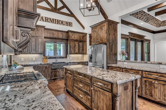 kitchen with beam ceiling, light stone countertops, a center island, an inviting chandelier, and high quality fridge