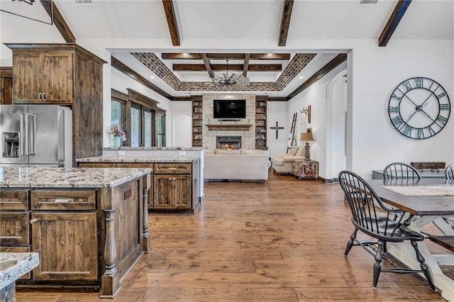 kitchen featuring light stone countertops, a fireplace, high quality fridge, beam ceiling, and wood-type flooring