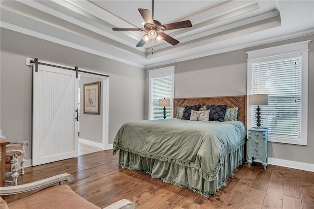 bedroom with ceiling fan, a barn door, a tray ceiling, multiple windows, and ornamental molding