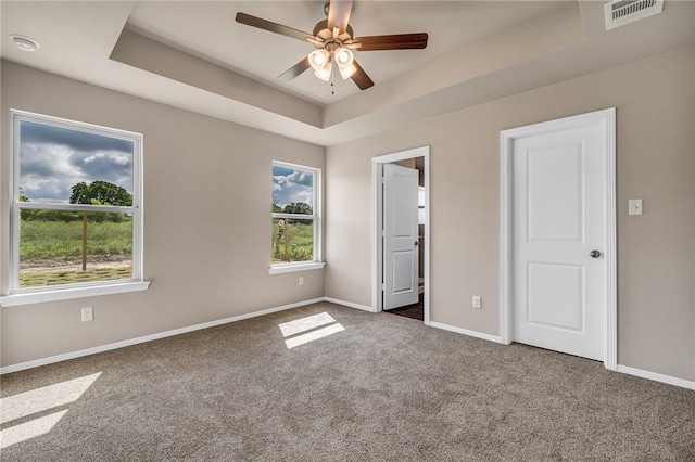 unfurnished room featuring carpet flooring, baseboards, visible vents, a tray ceiling, and ceiling fan