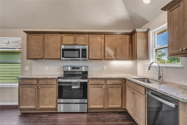 kitchen featuring stainless steel appliances, a sink, lofted ceiling, light stone counters, and dark wood-type flooring