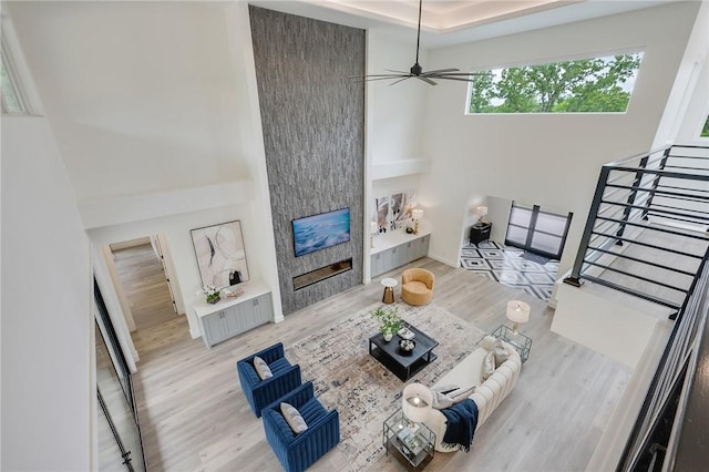 living room with a fireplace, wood finished floors, a high ceiling, and a ceiling fan